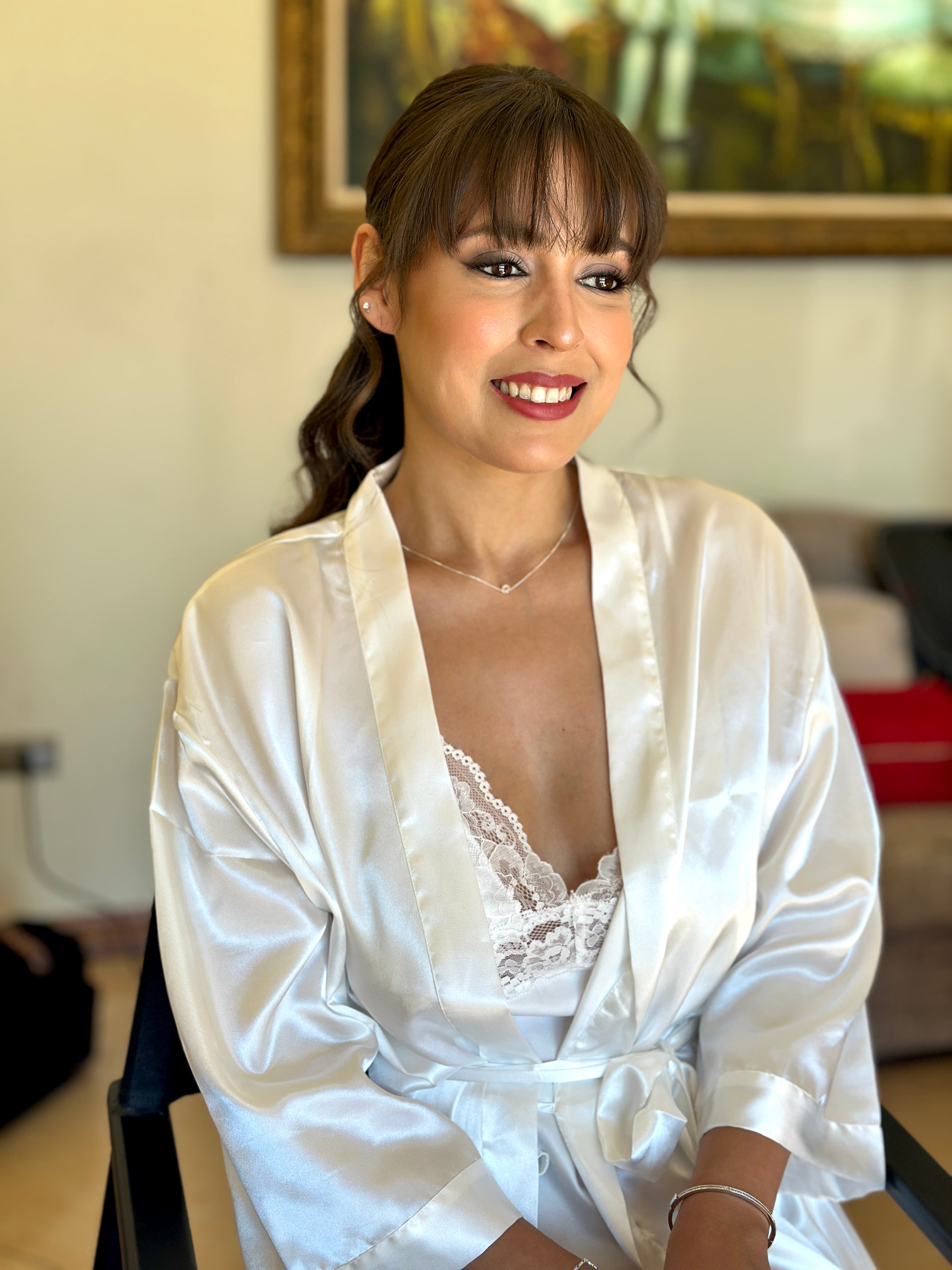 Novia de fiesta con bata de seda, coleta baja y labio berry